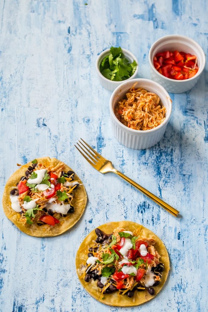 shredded chicken tacos with sour cream, cilantro, black beans, and salsa on them