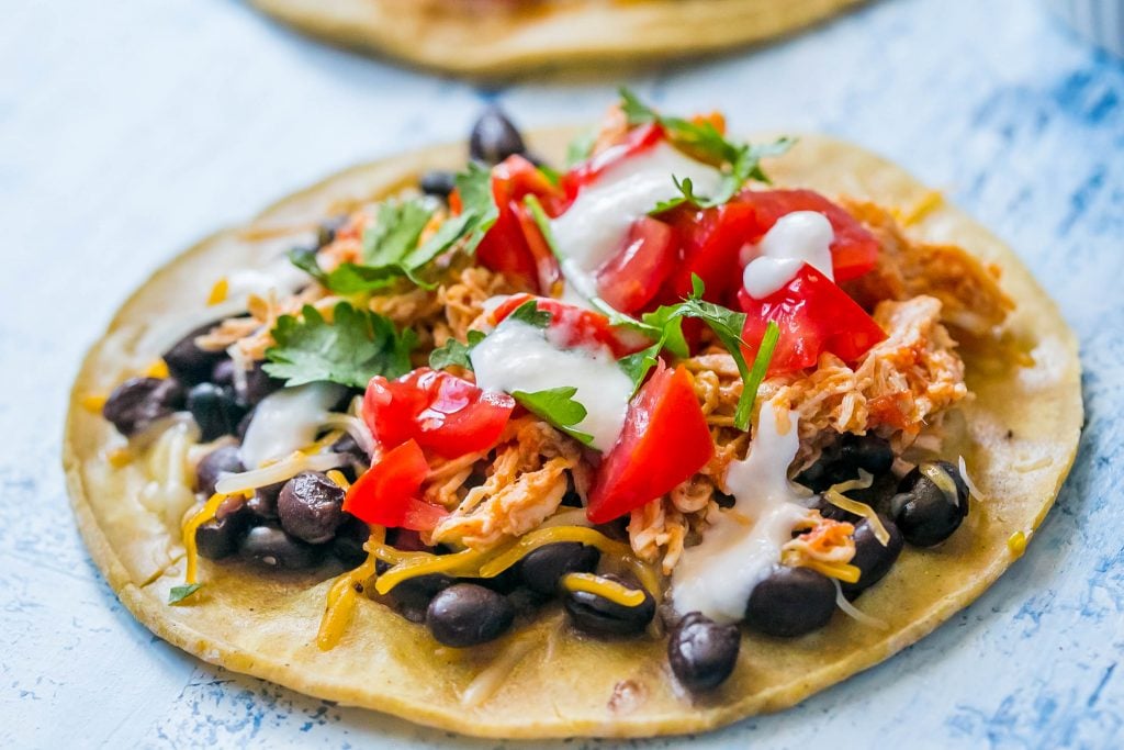 shredded chicken tacos with sour cream, cilantro, black beans, and salsa on them