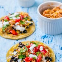 Two Mexican shredded chicken tacos on a blue background.