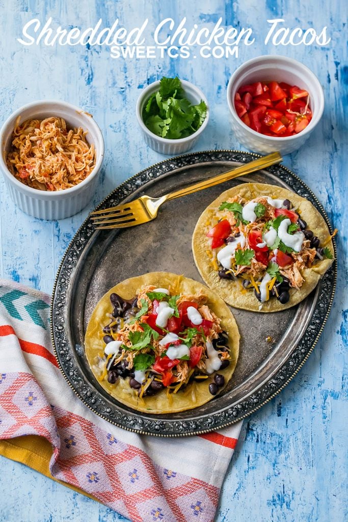 shredded chicken tacos with sour cream, cilantro, black beans, and salsa on them