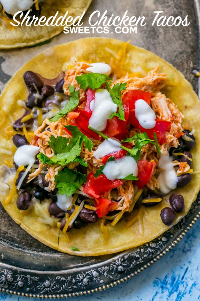 shredded chicken tacos with sour cream, cilantro, black beans, and salsa on them