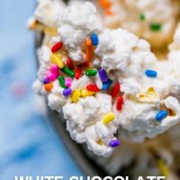 White chocolate popcorn with sprinkles in a bowl topped with cake batter.