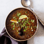 A bowl of Indian lentil soup with a spoon and lime.