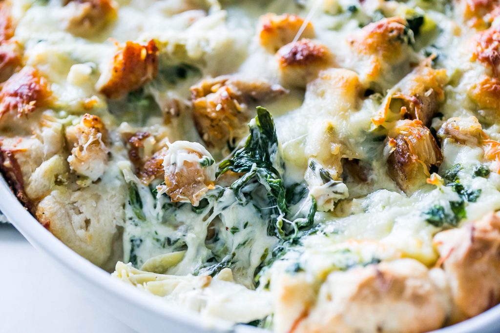 picture of cheesy chicken, spinach, and artichoke bread dip in a white casserole dish up close.  
