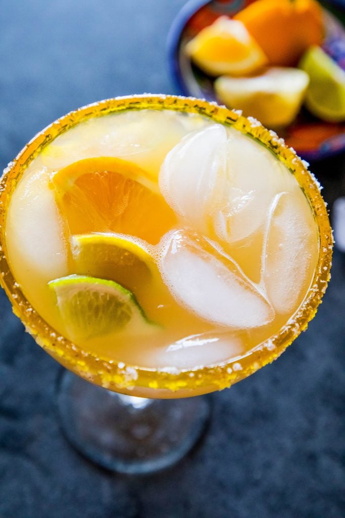 yellow margarita with lemon and lime wedges in it