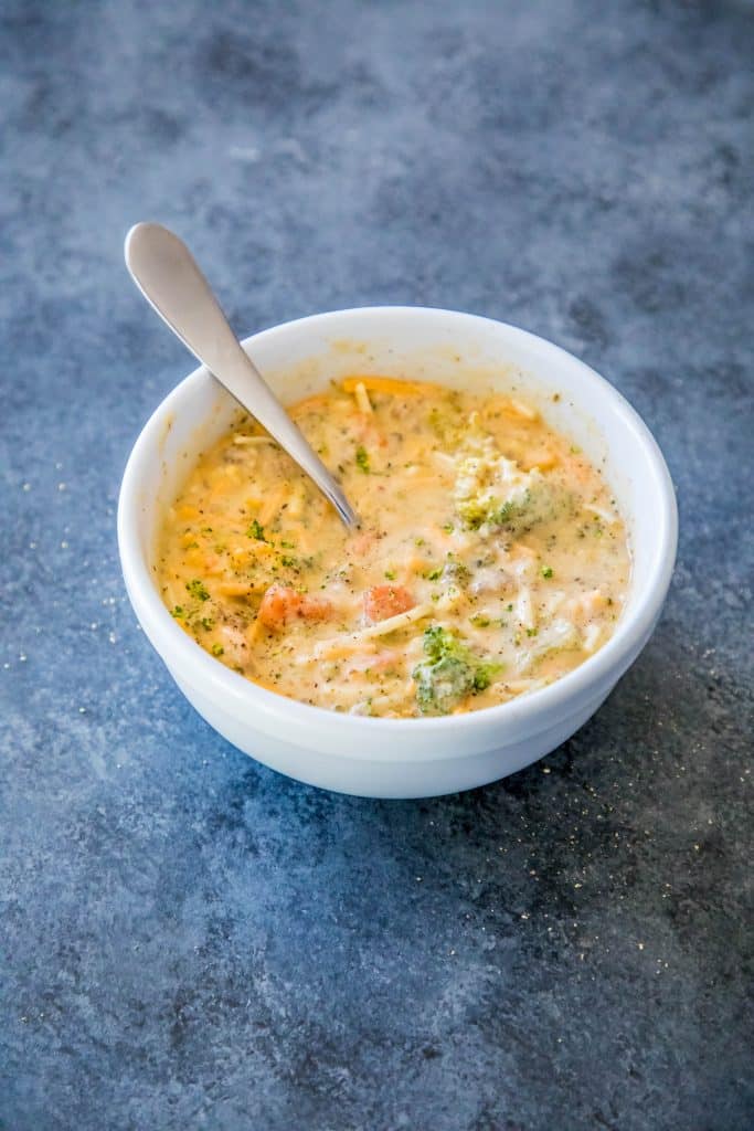 picture of creamy cheesy and broccoli soup in a white bowl with a spoon in it. 