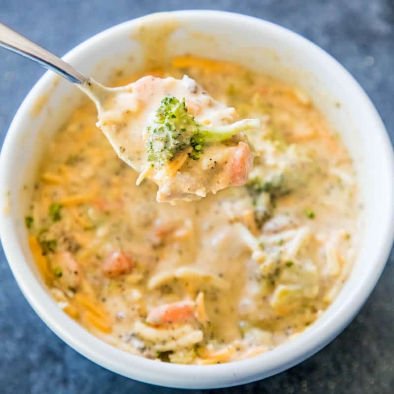 picture of creamy cheesy and broccoli soup in a white bowl with a spoon in it. 