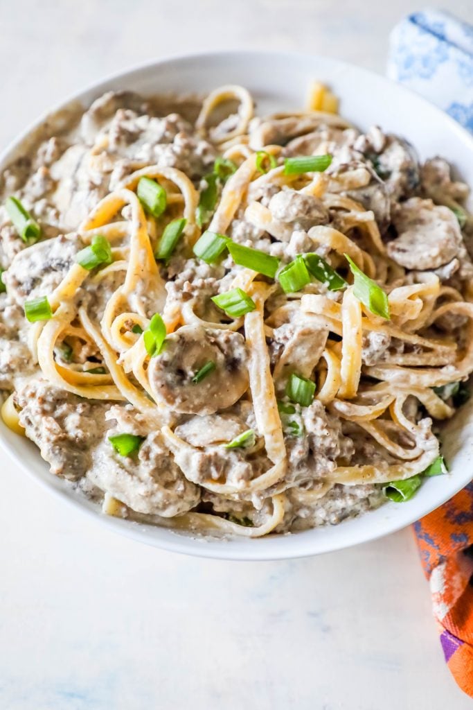 noodles with creamy stroganoff with mushrooms and chives on top sitting on a white plate