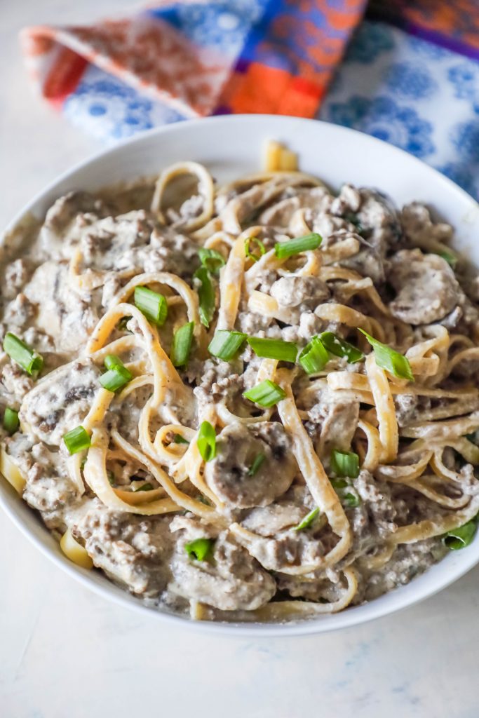 noodles with creamy stroganoff with mushrooms and chives on top sitting on a white plate