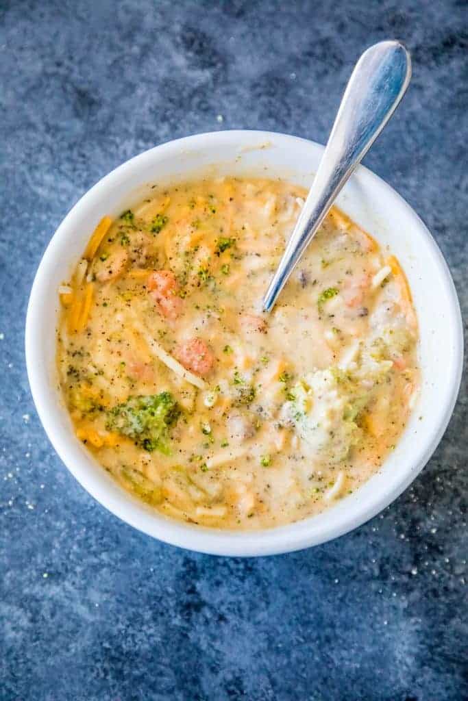 picture of creamy cheesy and broccoli soup in a white bowl with a spoon in it. 