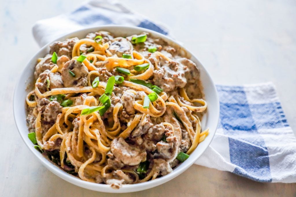 noodles with creamy stroganoff with mushrooms and chives on top sitting on a white plate