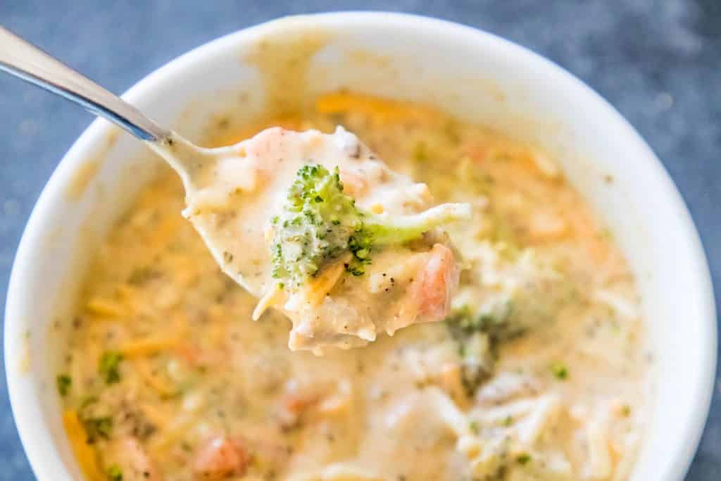 picture of creamy cheesy and broccoli soup in a white bowl with a spoon in it. 