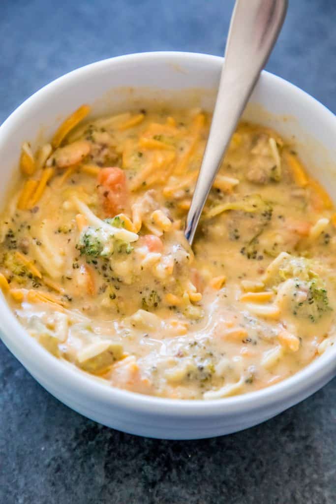 picture of creamy cheesy and broccoli soup in a white bowl with a spoon in it.