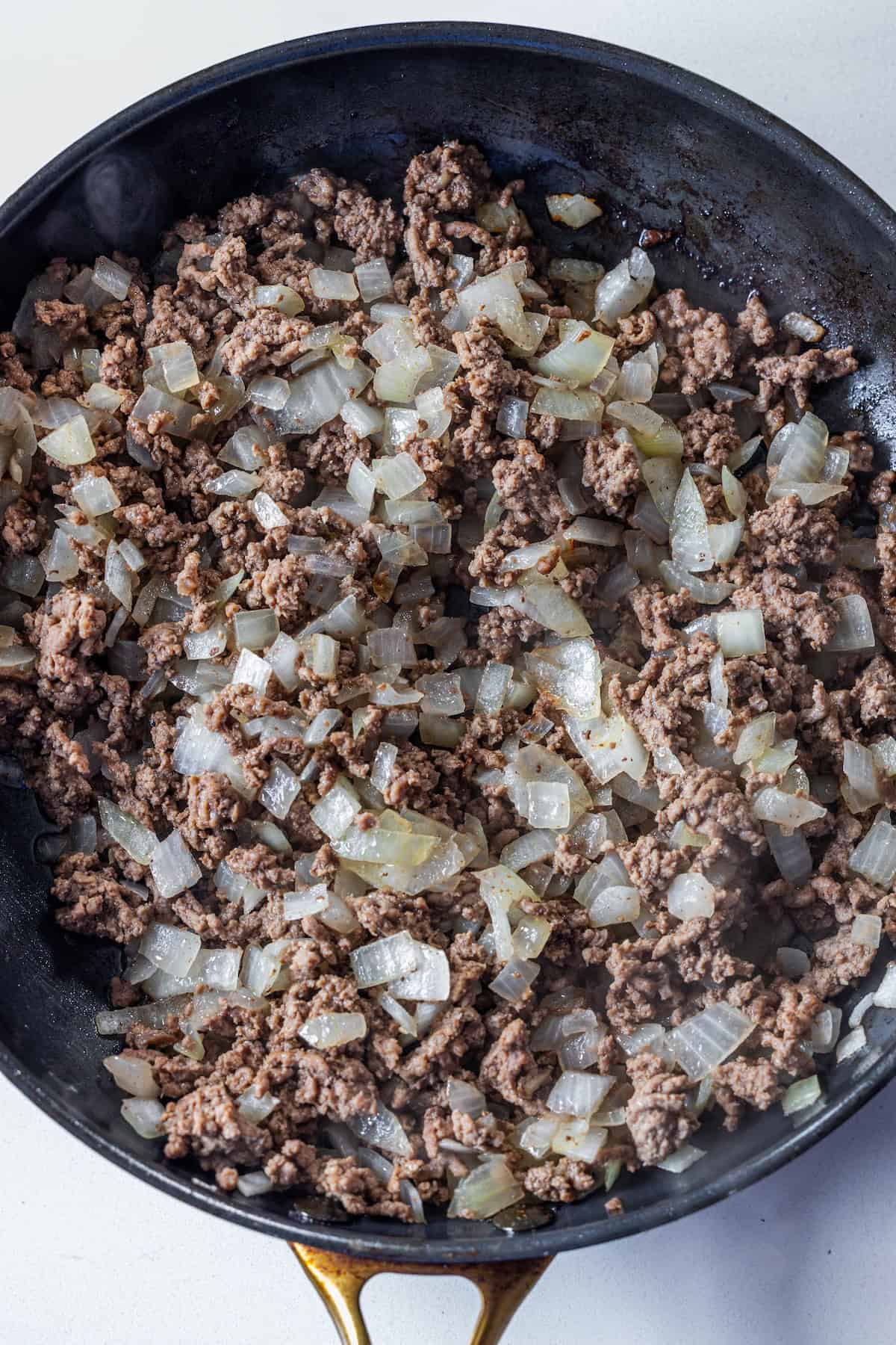 Cooked ground beef and diced onions in a black skillet, perfect as the savory base for Creamy Beef Stroganoff Fettuccine.