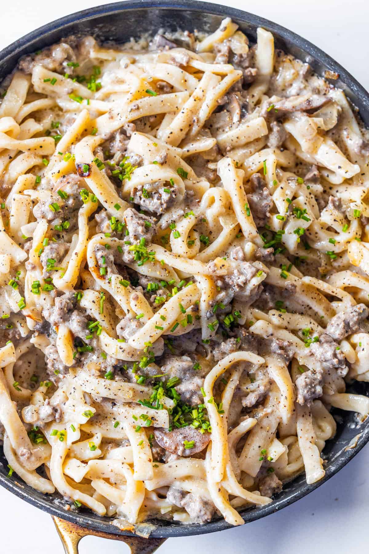 A skillet filled with creamy Beef Stroganoff Fettuccine, ground meat, and garnished with chopped herbs and black pepper.
