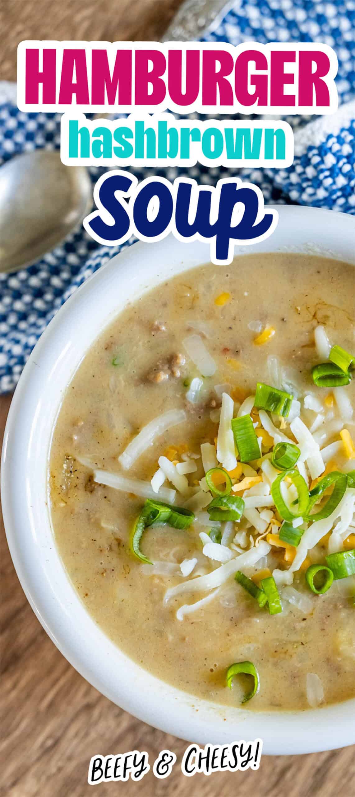 A bowl of creamy hash brown hamburger soup topped with shredded cheese and green onions, accompanied by a spoon and a blue patterned cloth napkin.