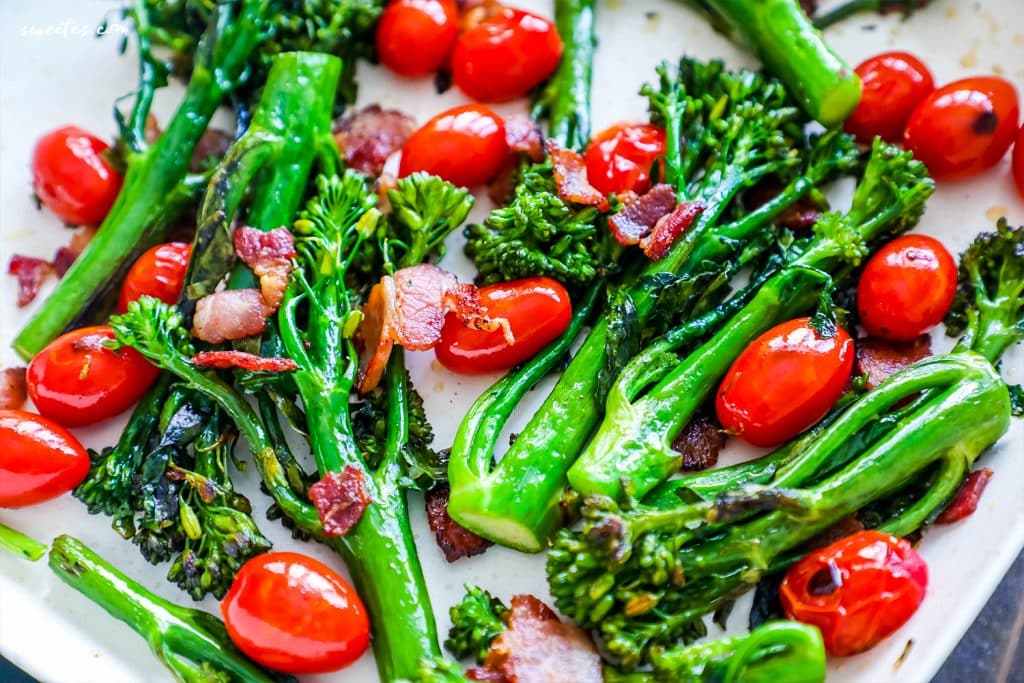 broccolini, cherry tomatoes, and bacon up close on a white plate. 