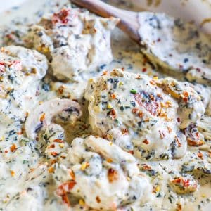 chicken in a dish with white sauce and red pepper flakes and mushrooms in it