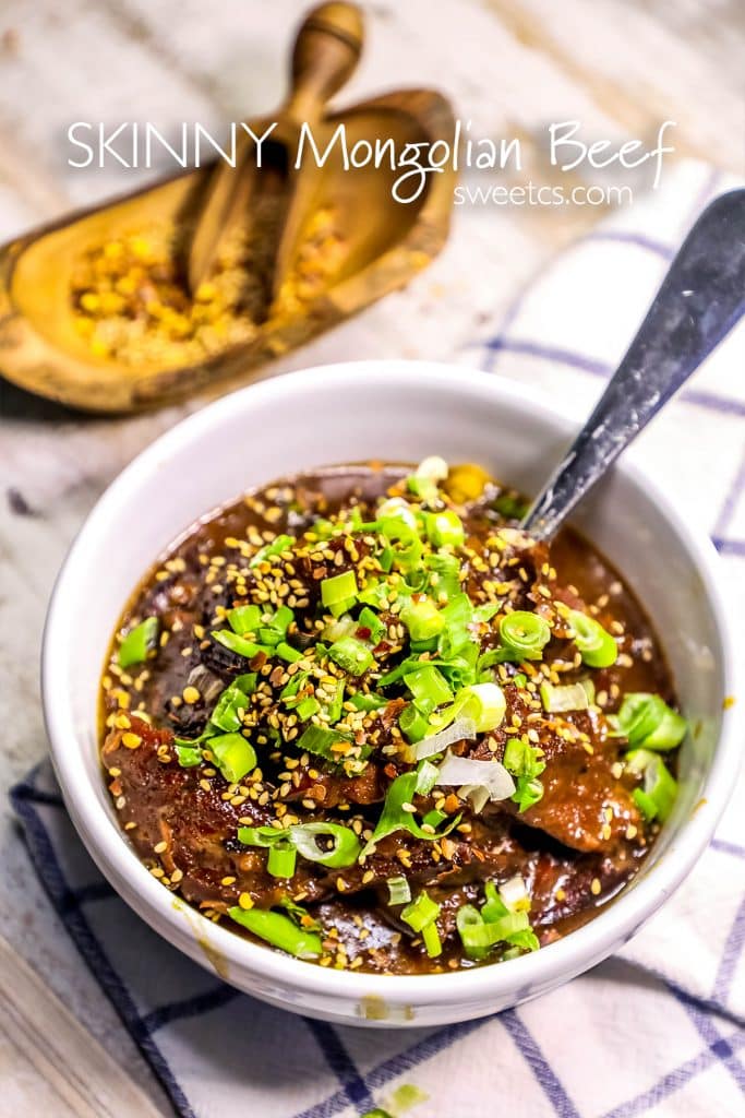 Mongolian beef stew in a bowl with green onions on it and a spoon in it with a towel in the background. 