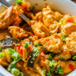 A close-up of a colorful Paleo Kung Pao Chicken and vegetable stir-fry dish in a white bowl, garnished with chopped green onions and red chili flakes.