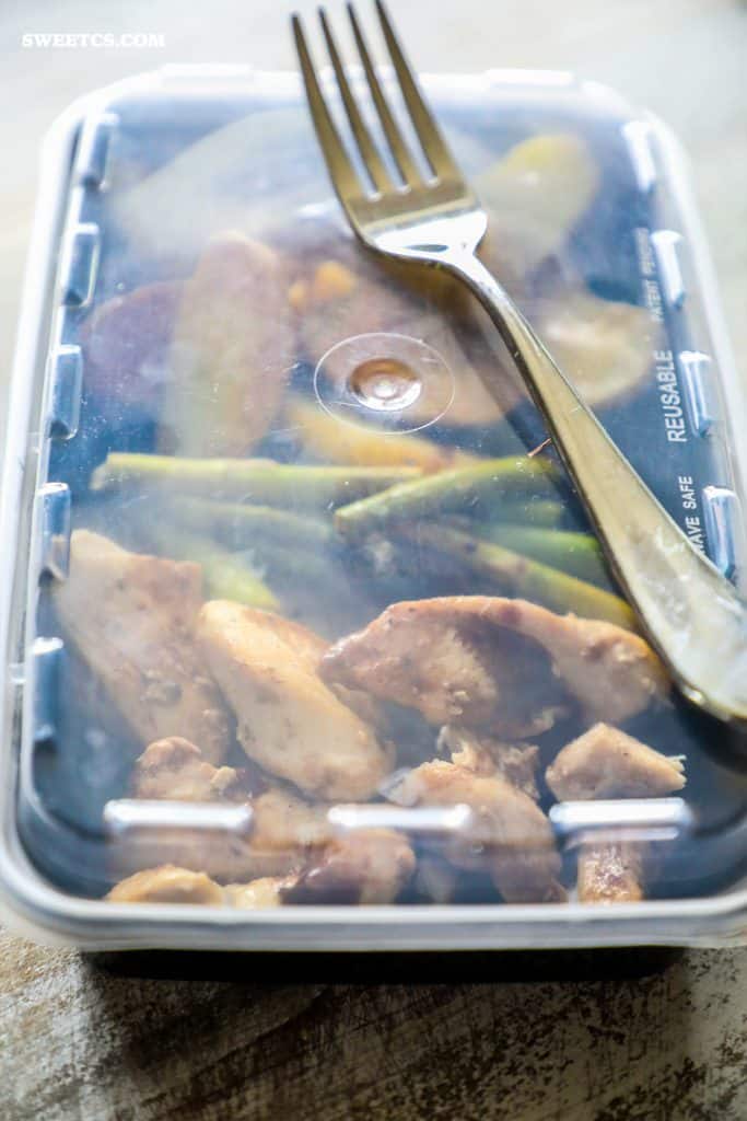 plastic container with roasted potatoes, asparagus, and cooked chicken in it covered with plastic top