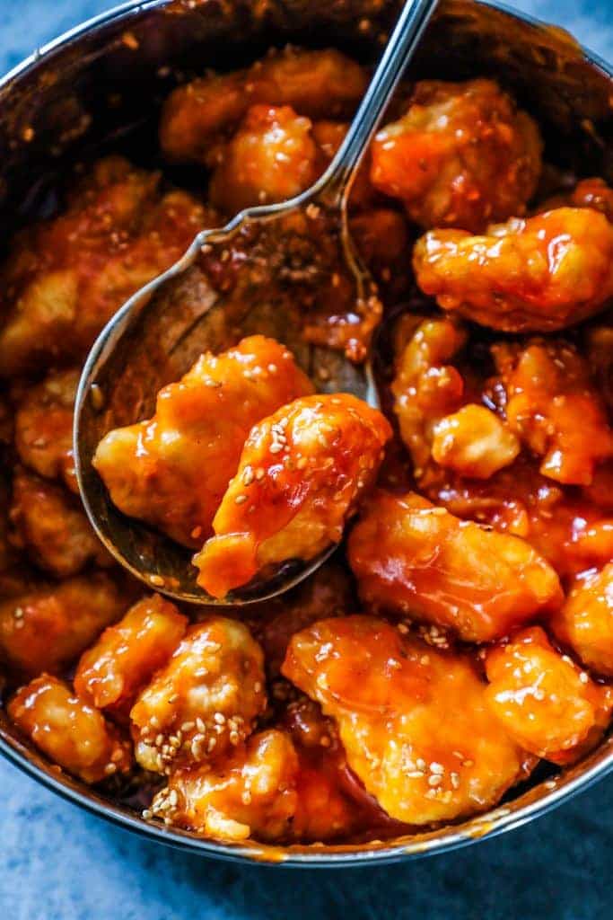 bowl of chicken with orange sauce and sesame seeds on it, one spooned