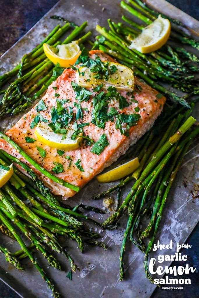 picture of salmon and asparagus on a baking sheet with lemons and parsley on top of it