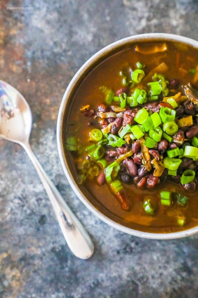 a bowl of black beans in a soup with green onions on it