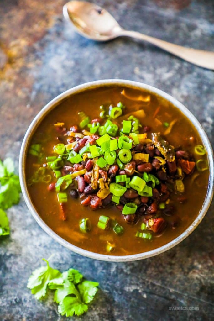 a bowl of black beans in a soup with green onions on it