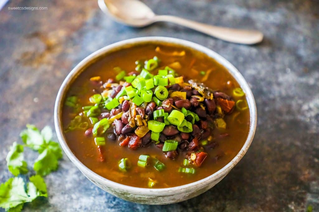 a bowl of black beans in a soup with green onions on it
