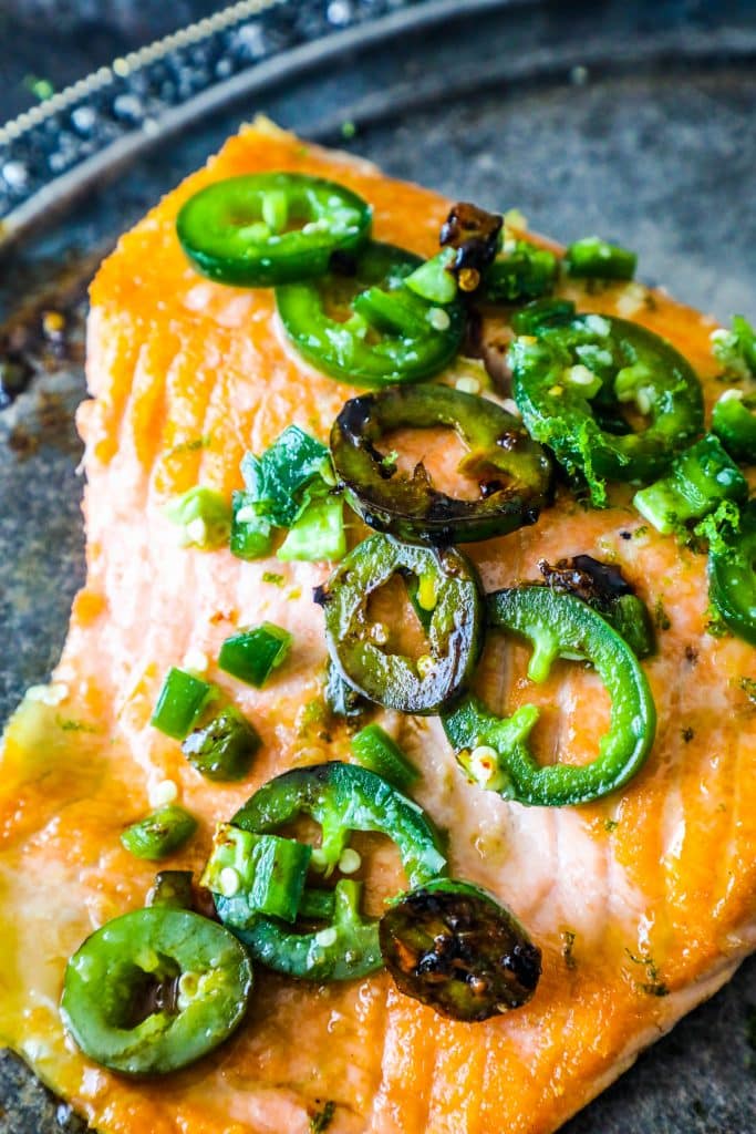 picture of salmon with jalapenos on it, limes on the side on a metal plate. 