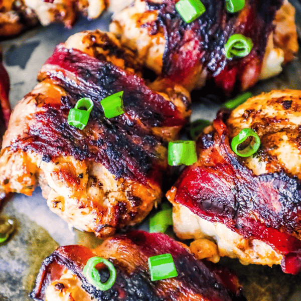 Bacon Balsamic Glazed Chicken Thighs are grilled to perfection, wrapped in crispy bacon, and garnished with chopped green onions on a tray.