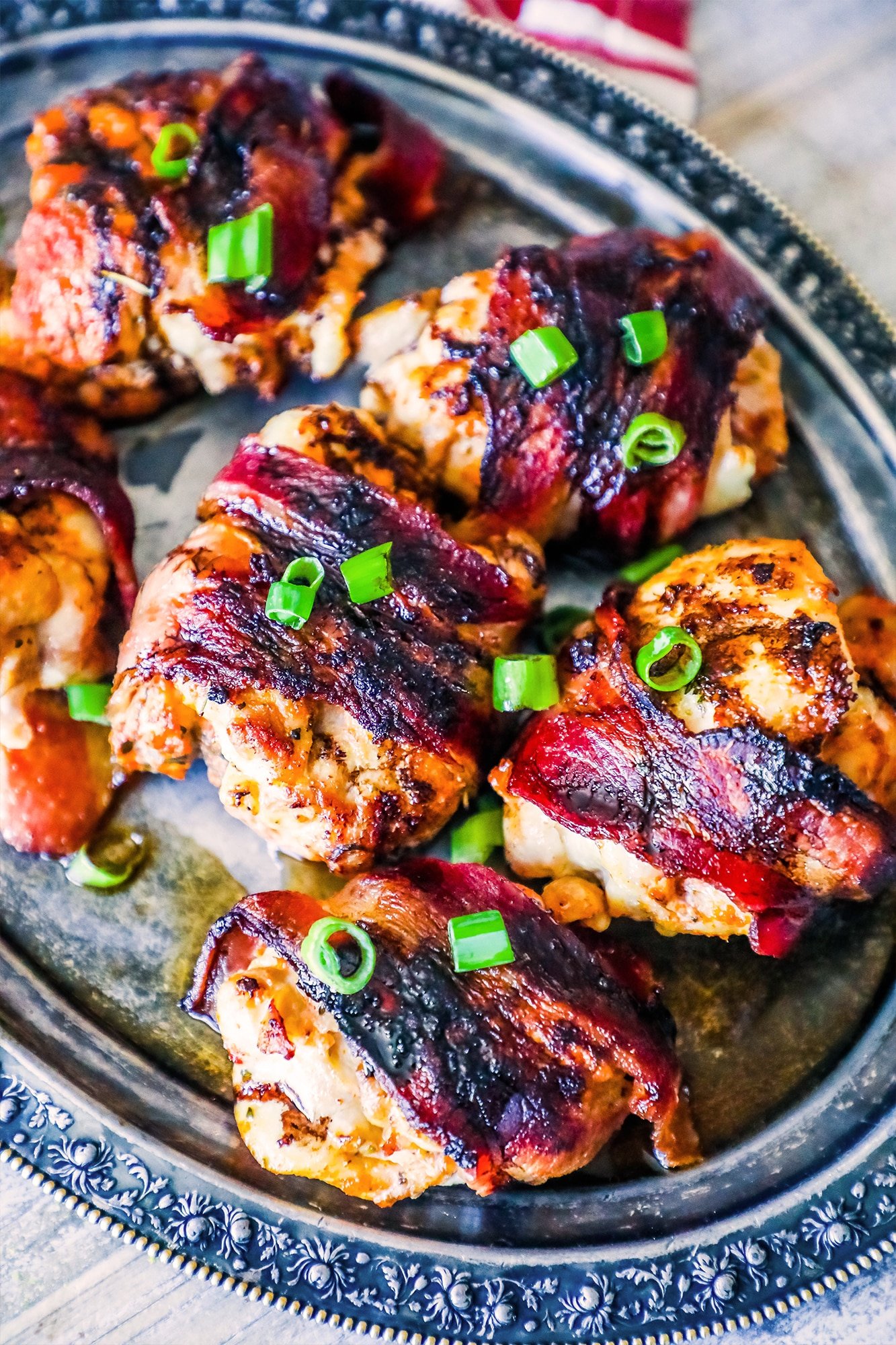 bacon wrapped chicken thighs on a silver plate with green onions on them. 