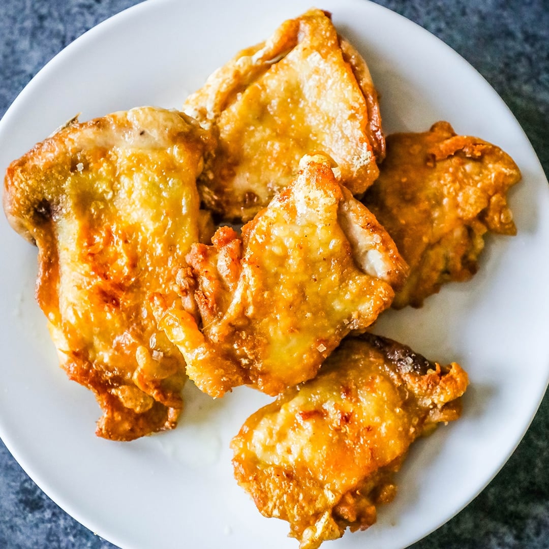 Pan fried chicken thighs on a white plate without breading.