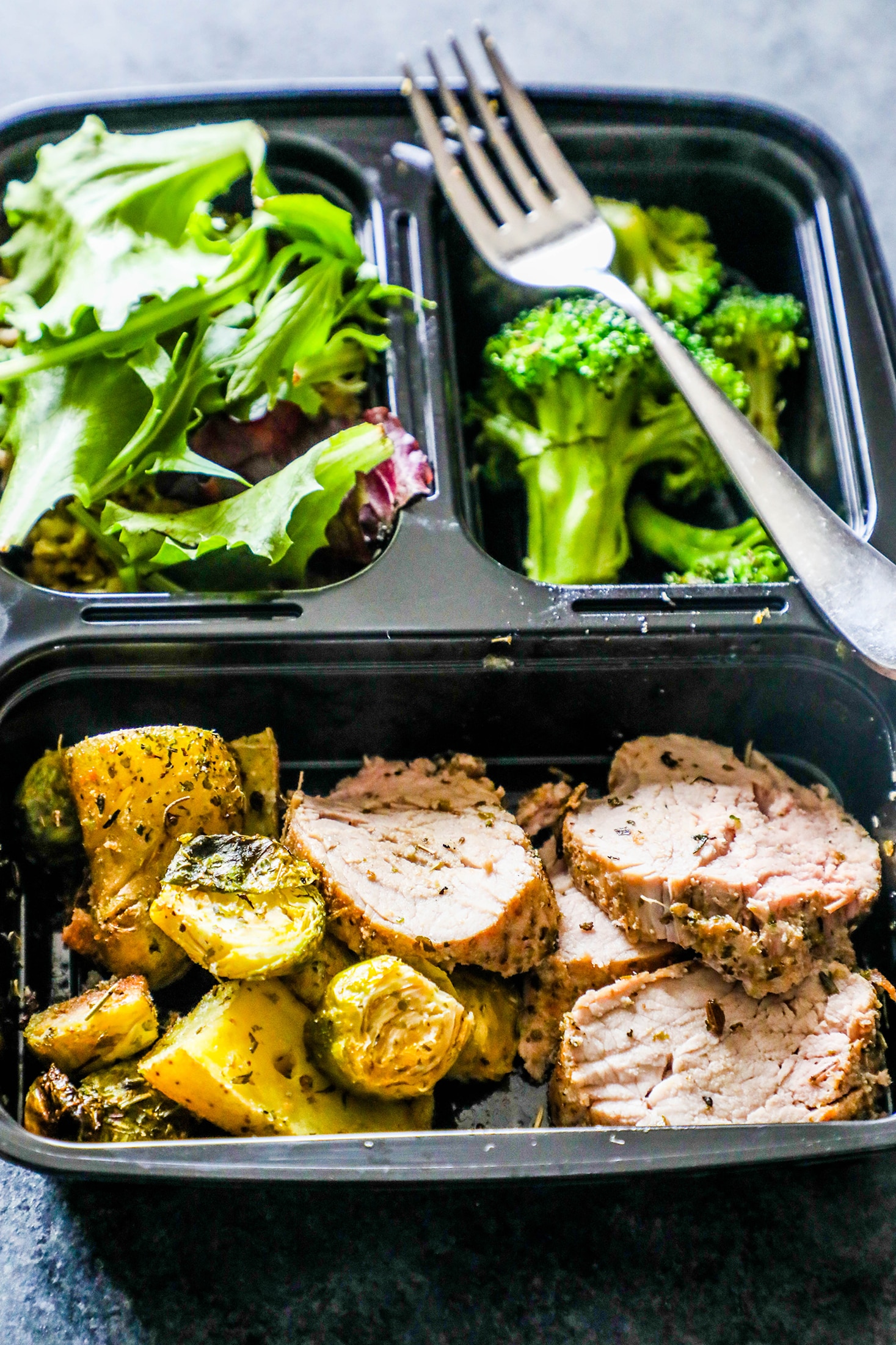 pork covered in italian herbs and veggies on the side sliced in a container with salad and broccoli