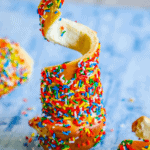 Colorful sprinkles covering a caramel-coated marshmallow with a bite taken out of the sprinkle chimney cake.