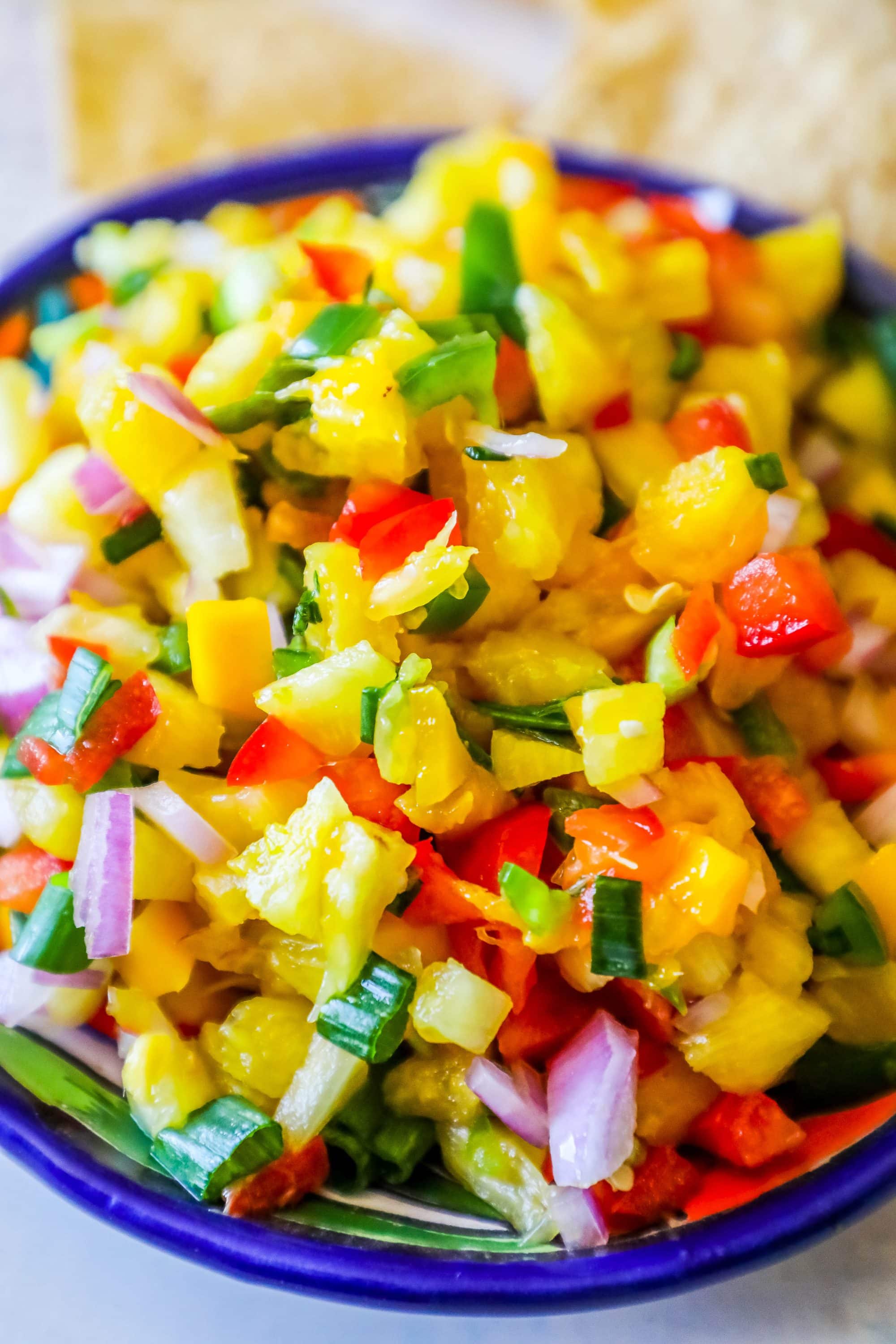 bowl with pineapple, jalapeno, red onion, and green onions, chips behind it