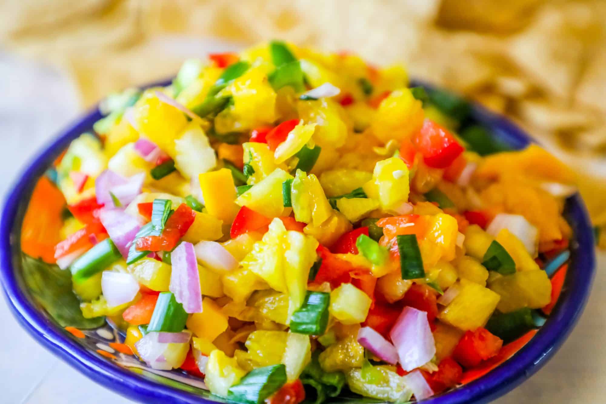 bowl with pineapple, jalapeno, red onion, and green onions, chips behind it