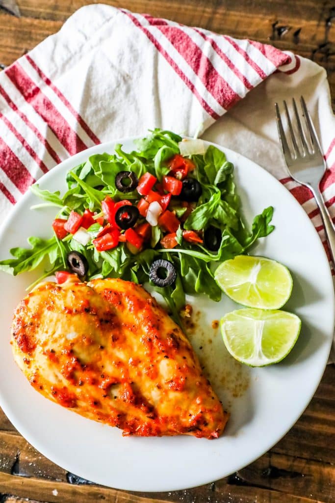 chicken, a salad with olives and tomatoes, and limes on a plate