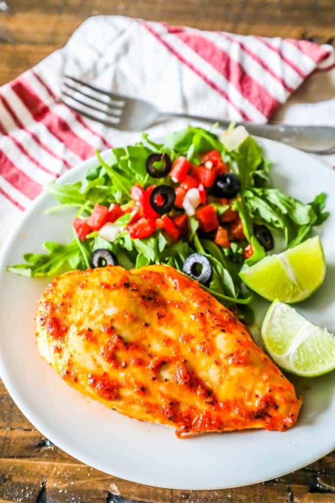 chicken, a salad with olives and tomatoes, and limes on a plate