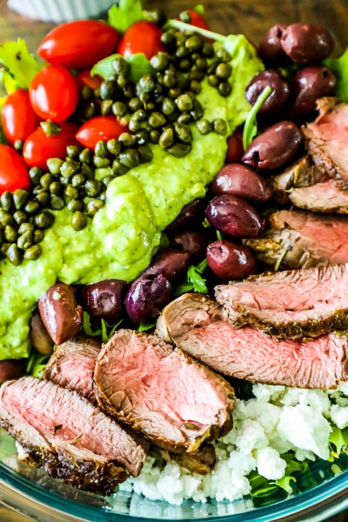 bowl of steak, capers, tomatoes, olives, cheese, and lettuce with green dressing