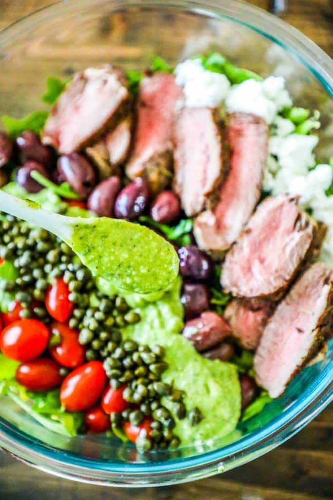 bowl of steak, capers, tomatoes, olives, and lettuce with green dressing