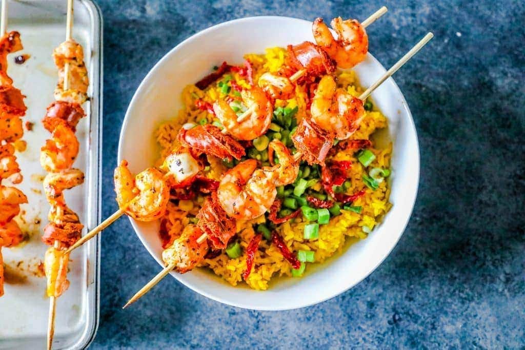 shrimp on a skewer over yellow rice with sundried tomatoes and green onions