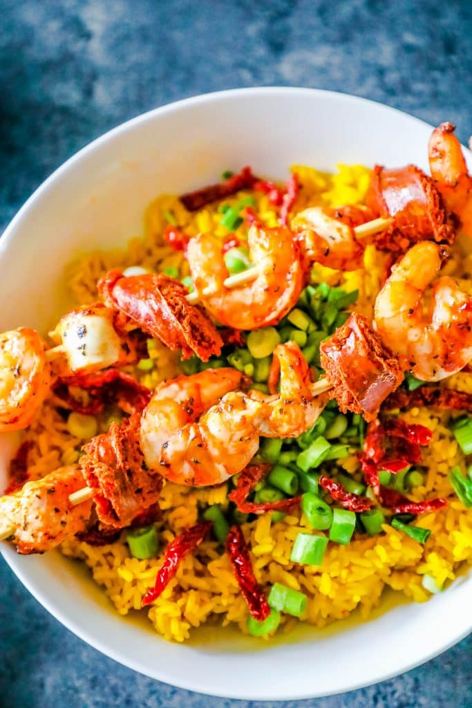 shrimp on a skewer over yellow rice with sundried tomatoes and green onions