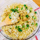 A bowl of cauliflower rice with green onions and a wooden spoon.