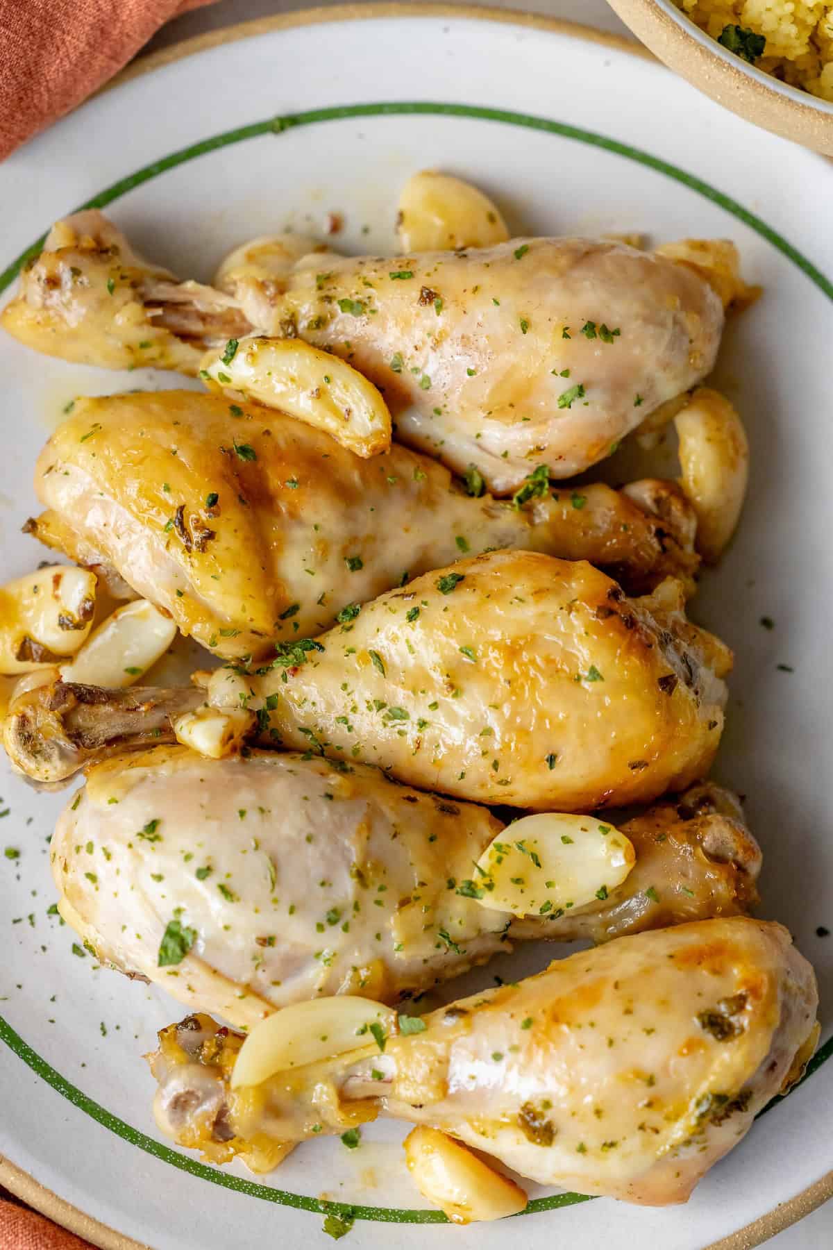 A plate of Greek chicken drumsticks garnished with aromatic herbs and garlic cloves.