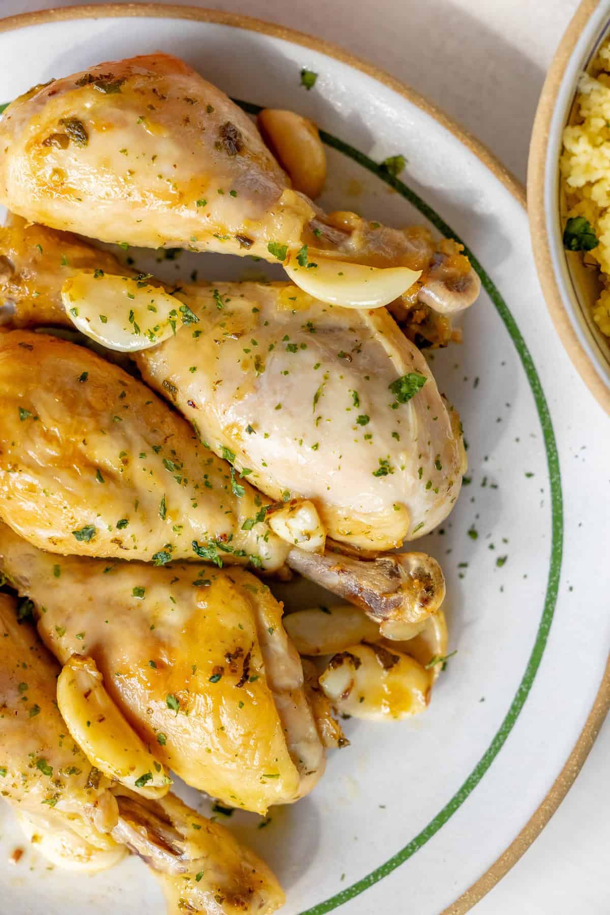 Plate of seasoned and roasted Greek chicken drumsticks with garlic cloves, garnished with herbs.