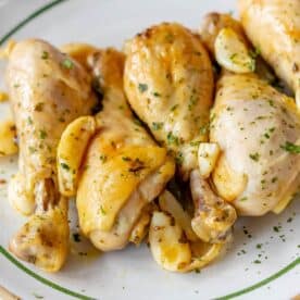 A plate of Greek chicken drumsticks garnished with fresh herbs and garlic cloves offers a savory Mediterranean delight.