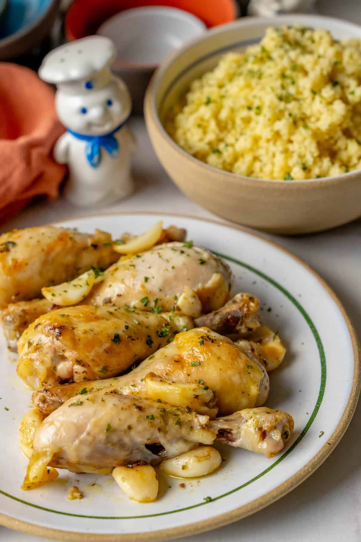 A plate of Greek chicken drumsticks with garlic and herbs, served alongside a bowl of fluffy couscous.