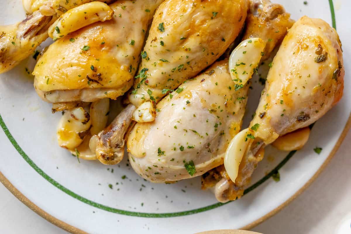 Plate of Greek chicken drumsticks roasted to perfection, garnished with fragrant garlic and freshly chopped herbs.